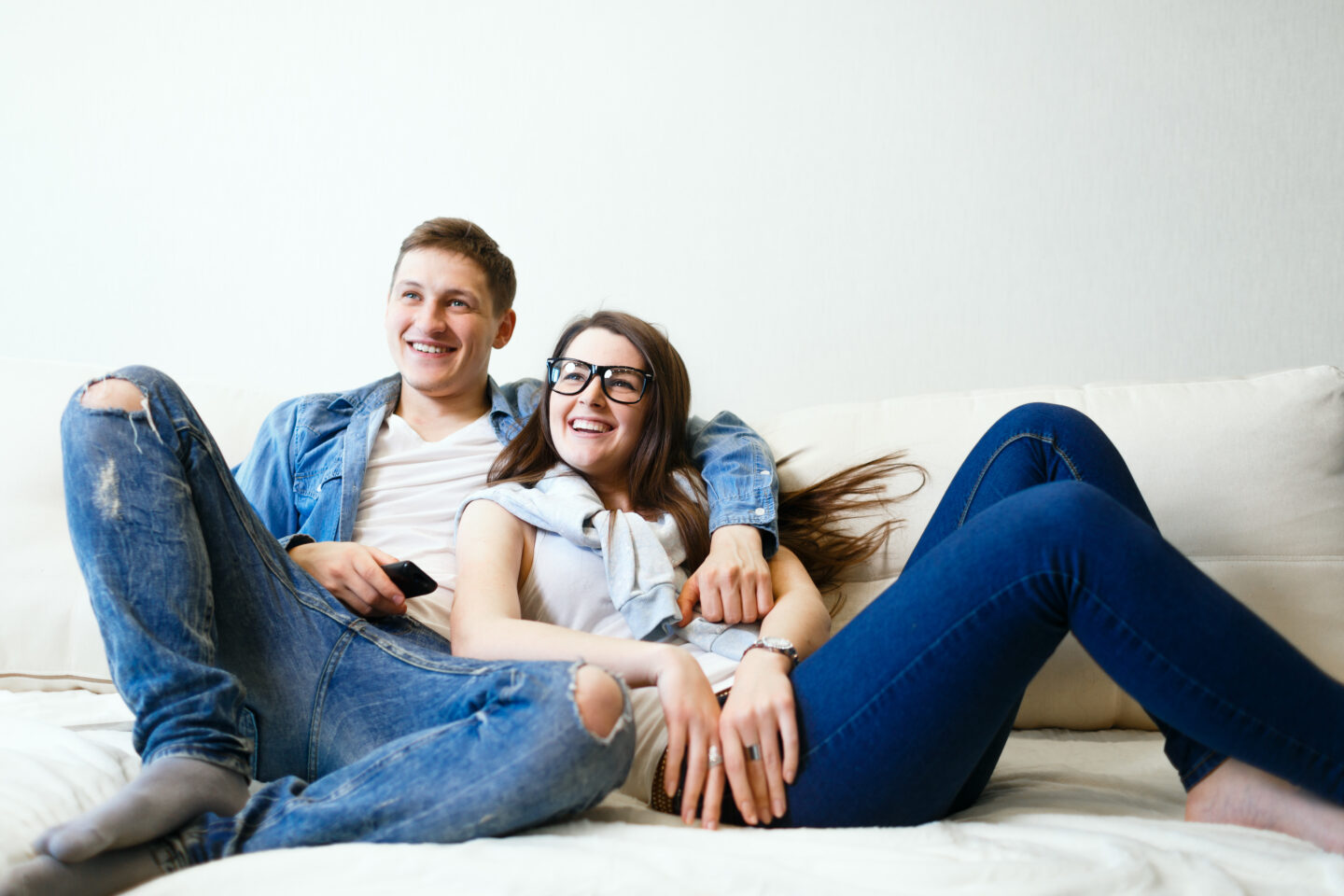 Young couple husband and wife sitting on sofa watching TV and smiling